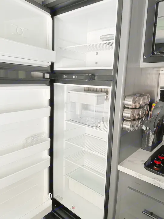 Clean, empty RV rental refrigerator and freezer. Visible shelves, a Brita filter, and part of the RV kitchen with magnetic spice jars.. Dutchmen Other 2021