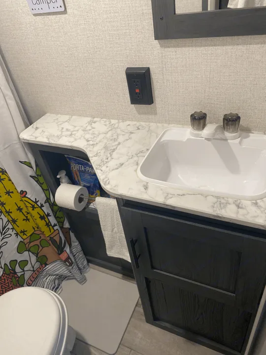 Clean RV rental bathroom featuring a compact sink, marble-pattern counter, and open storage for travel essentials.. Dutchmen Other 2021