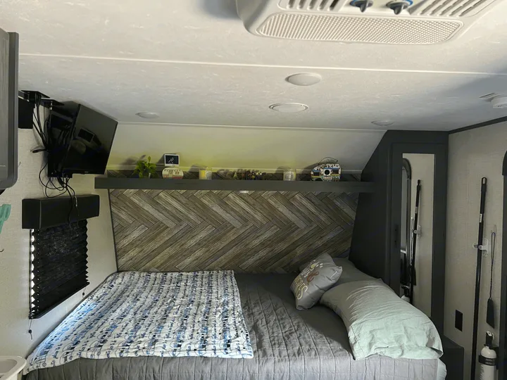 Cozy RV rental bedroom featuring a herringbone wall, comfy bed, mounted TV, and organized essentials.. Dutchmen Other 2021