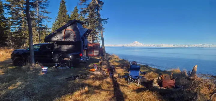 Truck with rooftop camper, an ideal RV rental, enjoys serene waterfront views of snow-capped mountains. A peaceful camping spot.. Toyota Tacoma 2022