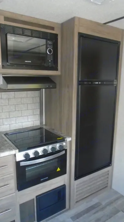 Efficient RV rental kitchen featuring built-in microwave, four-burner stovetop, oven, and tall refrigerator.. Crossroads RV Zinger 2022