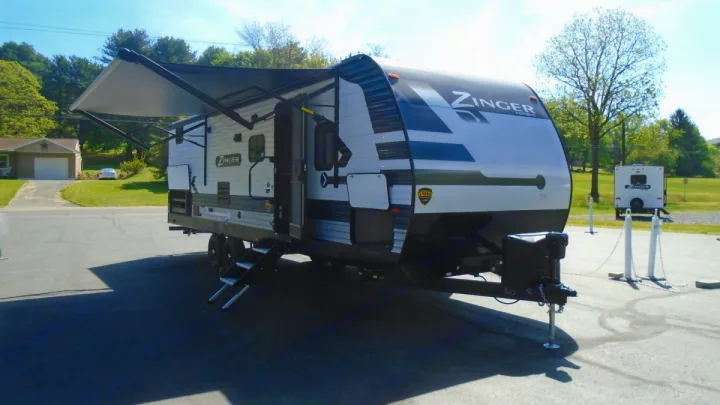 A white and black Zinger travel trailer with an extended awning, steps down, on an asphalt lot, ideal for an RV rental.. Crossroads RV Zinger 2022