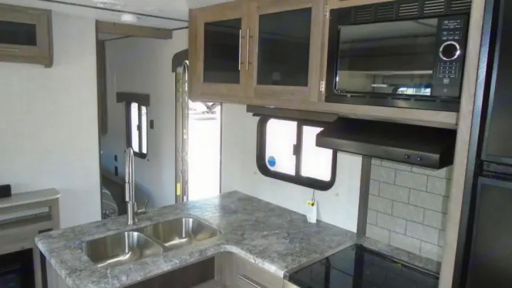 Modern RV rental kitchen with double sink, microwave, upper cabinets, and stove, ready for your adventures.. Crossroads RV Zinger 2022