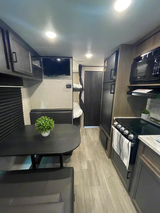 Modern RV rental interior showing a compact kitchen, dining area, bunk beds, and entertainment setup.. Jayco Jay Flight 2022