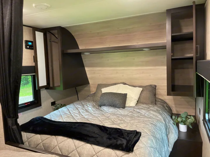 A well-appointed RV rental bedroom, featuring a comfortable bed, overhead storage, and light wood-look wall panels.. Jayco Jay Flight 2022