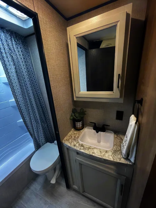 Modern RV rental bathroom with a compact shower/tub, toilet, and stylish vanity featuring a sink, black faucet, & mirror.. Jayco Jay Flight 2022