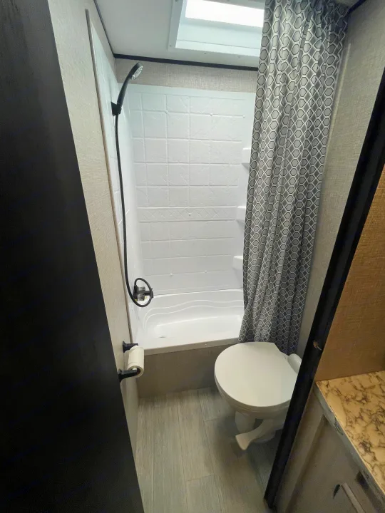 Inside an RV rental: a compact bathroom with a white tub/shower, toilet, and patterned curtain.. Jayco Jay Flight 2022