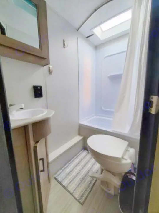 Inside a compact RV rental bathroom, a toilet, sink, shower, and bright skylight are visible, ready for travel.. Keystone RV Hideout Luxury 2021