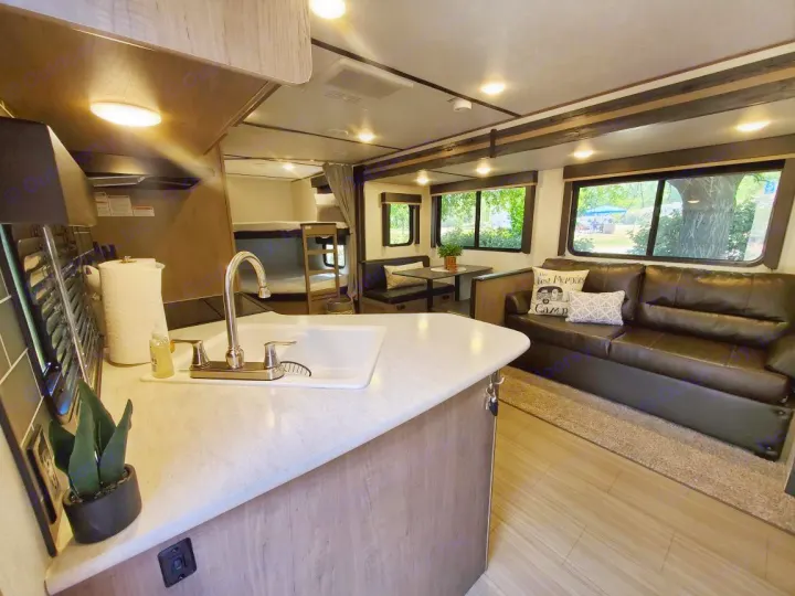 Spacious RV rental interior showcasing a full kitchen, living area with a dark sofa, dining nook, and bunk beds.. Keystone RV Hideout Luxury 2021