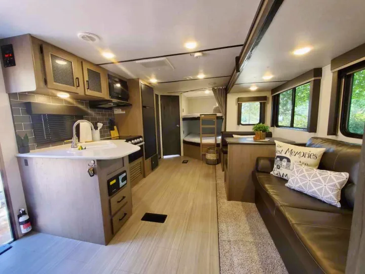 Spacious RV rental interior showing a modern kitchen island, comfy sofa, dining area, and bunk beds. Ready for your trip!. Keystone RV Hideout Luxury 2021