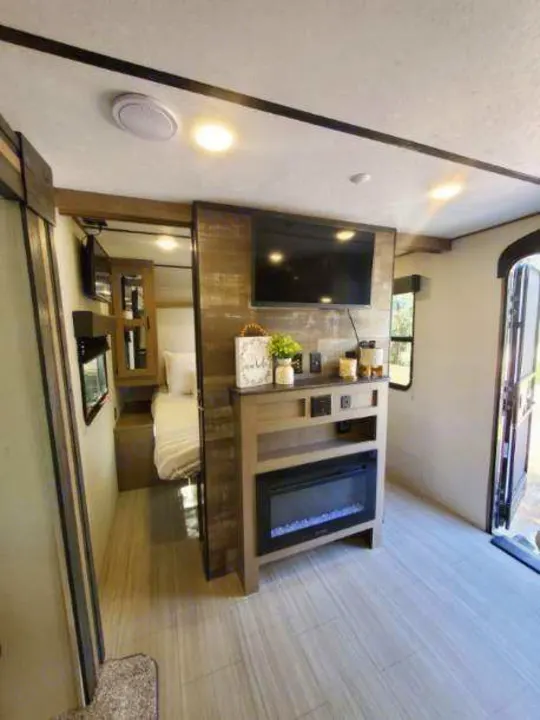 Spacious RV rental interior features a cozy living area with TV and fireplace, connected to a comfortable bedroom.. Keystone RV Hideout Luxury 2021