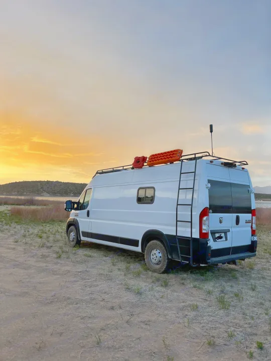 This white RV rental van, equipped for adventure, sits by a serene lake under a vibrant sunset, perfect for a Texas road trip.. Other Other 2021