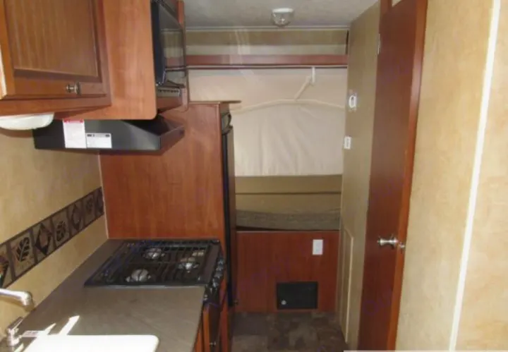 RV rental interior showing a compact kitchen with stove, sink, microwave, and a cozy pop-out sleeping area.. Jayco Jay Feather Ultra Lite 2012