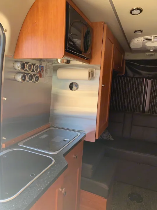 Compact RV rental interior featuring a kitchen with microwave, sinks, and a comfortable seating area.. Roadtrek Roadtrek Class B 2018