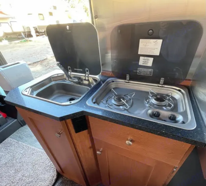 An RV rental's compact kitchenette: stainless steel sink & two-burner stove on dark counters, with wood cabinets below.. Roadtrek Roadtrek Class B 2018
