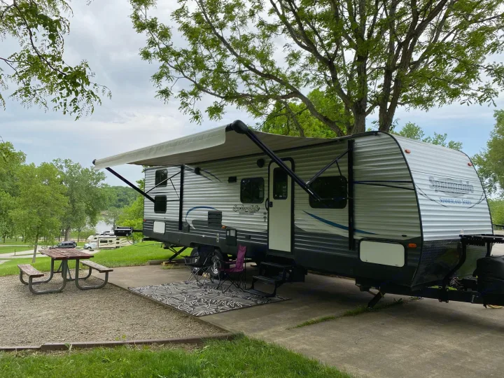 Enjoying nature with this RV rental set up at a scenic campsite, featuring an extended awning, picnic table, and chairs by the water.. Keystone RV Summerland 2018