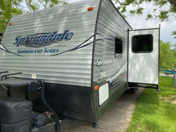 Grey Springdale Summerland Series RV rental travel trailer with open slide-out, parked on concrete at a sunny campsite.. Keystone RV Summerland 2018