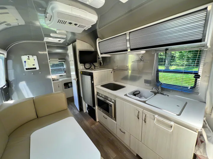 This inviting RV rental interior showcases a full kitchen, dining area with a sofa, and bright, modern design.. Airstream Sport 2019