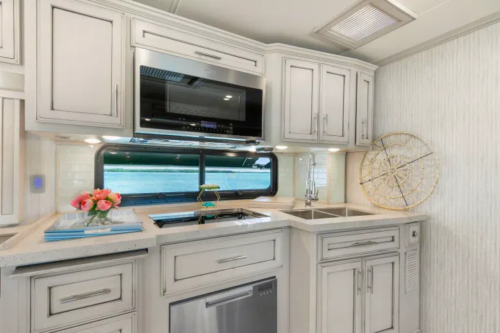 Bright RV rental kitchen with microwave, sink, stovetop, and white cabinets overlooking a scenic water view.. Ventana Ventana Motorhome 2022