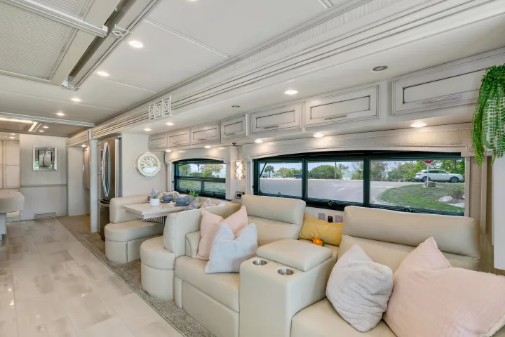 Spacious, modern RV rental interior featuring cream sofas, a dining booth, and large windows overlooking an ocean and road scene.. Ventana Ventana Motorhome 2022