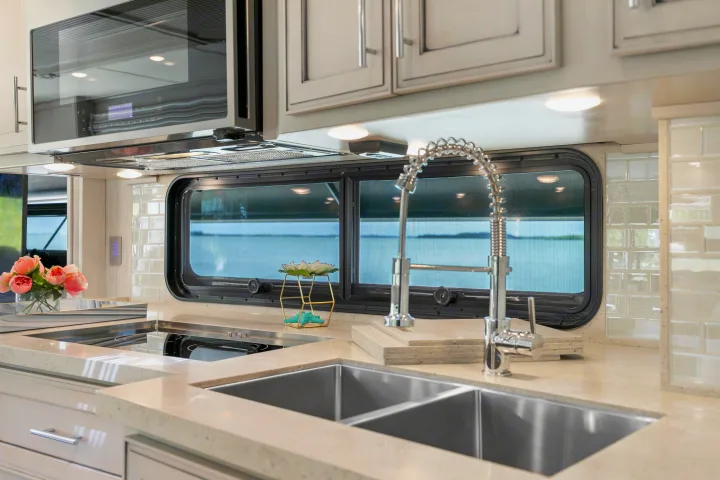 Modern RV kitchen featuring a large double sink, induction cooktop, microwave, and scenic water views. Ideal for any rv rental.. Ventana Ventana Motorhome 2022