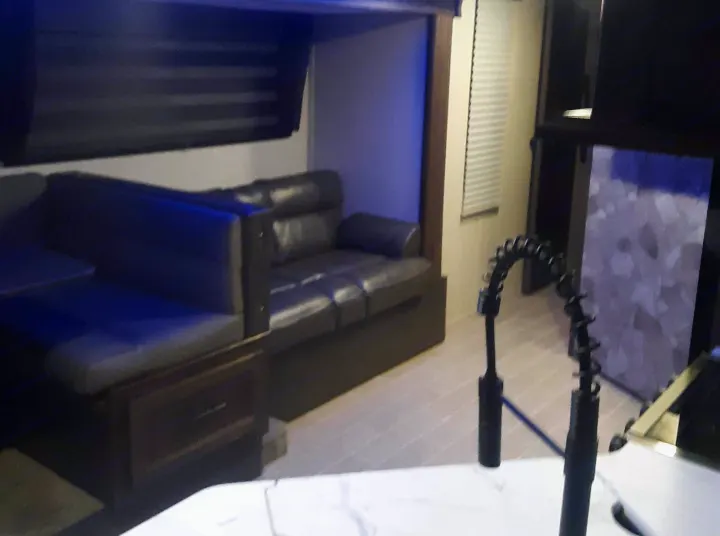 Inside a modern RV rental: a comfy dinette, leather sofa, and kitchen area are illuminated by ambient blue lighting.. Forest River Cherokee Grey Wolf 2020