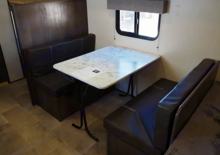 Spacious RV rental dinette featuring dark upholstered booths, a white marble table, and a window.. Coleman Coleman Lantern 2022