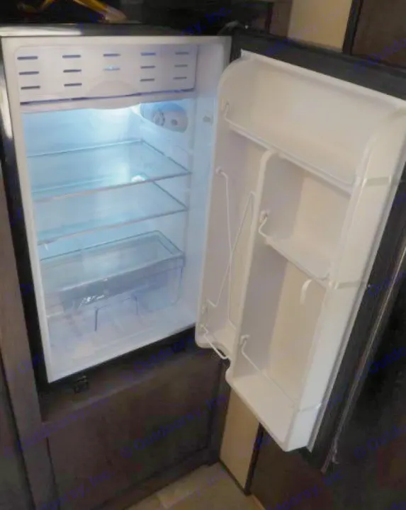 Inside view of an empty compact refrigerator in an RV rental, featuring clear shelves, a top freezer, and crisper drawer.. Coleman Coleman Lantern 2022
