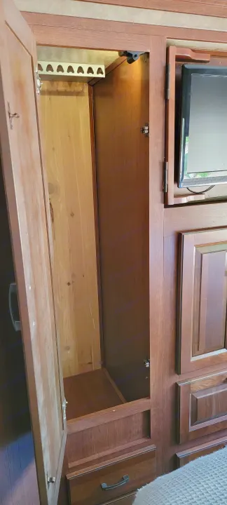RV rental interior: Open wood storage cabinet, cedar-lined, with light and heart-shaped rack, below a mounted TV.. Forest River 3171DS 2016