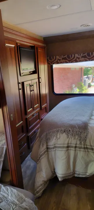 Inside a cozy RV rental bedroom featuring a bed, mounted TV, and wooden storage.. Forest River 3171DS 2016