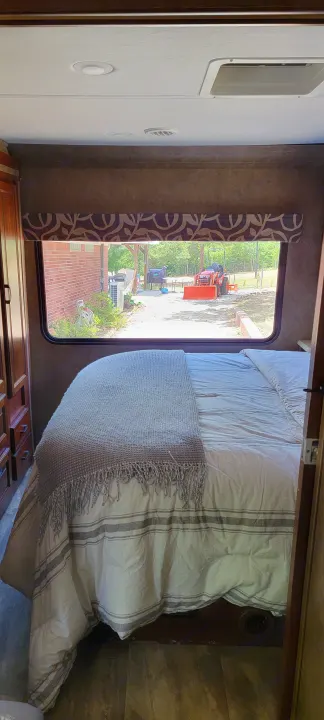 RV rental bedroom: cozy bed with outdoor view of a tractor and trees. Ideal for a nature getaway.. Forest River 3171DS 2016