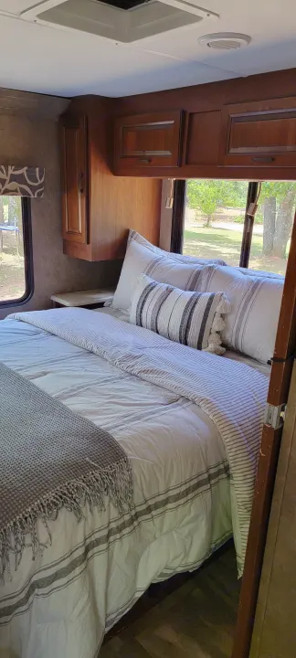 Interior of a comfortable RV rental bedroom, featuring striped bedding, wooden cabinets, and a scenic window view.. Forest River 3171DS 2016