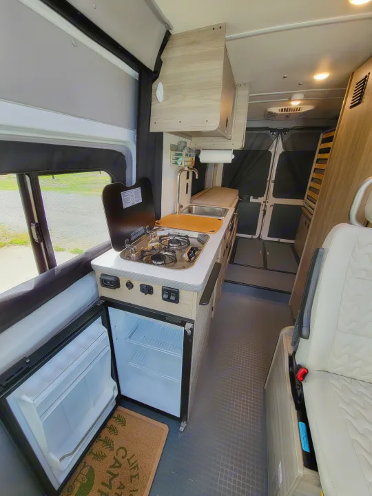 Spacious RV rental interior with a bright kitchen, open fridge, and living area. Ideal for road trips & camping.. Winnebago Solis 2021