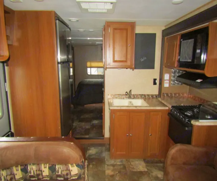 RV rental interior: kitchen with stove & sink, living area couch, and bedroom view, featuring wood-look flooring.. Coachmen Leprechaun 2017
