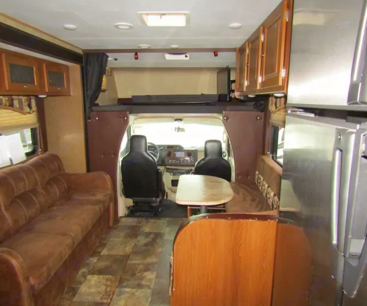 RV rental interior featuring a brown sofa, dining area, kitchen, and overhead bunk bed in a spacious layout.. Coachmen Leprechaun 2017