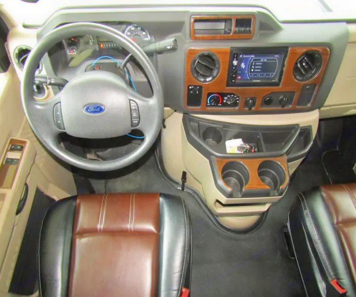 View of an RV rental cockpit: Ford steering wheel, dashboard with infotainment, and spacious front seats.. Coachmen Leprechaun 2017