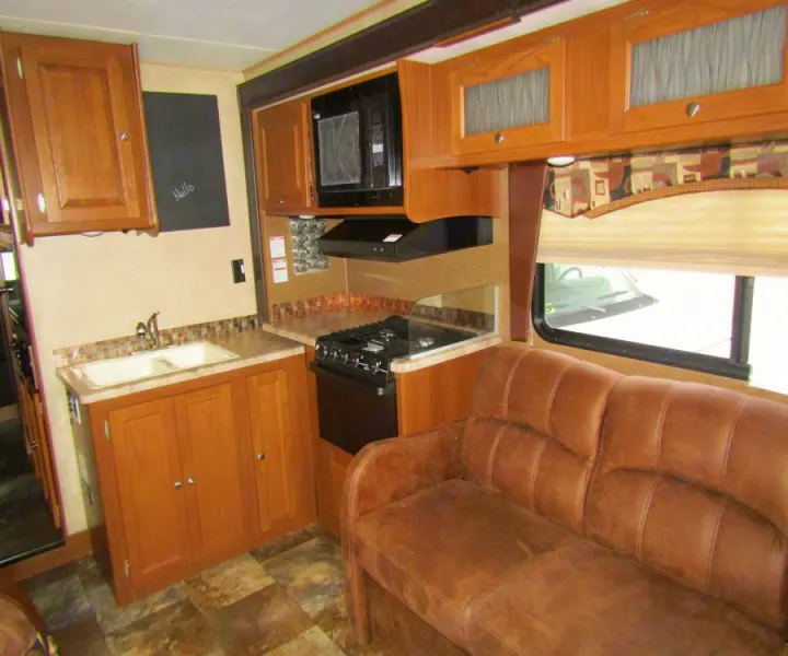 Cozy RV rental interior featuring a compact kitchen with a double sink, stove, microwave, and a comfy brown sofa.. Coachmen Leprechaun 2017