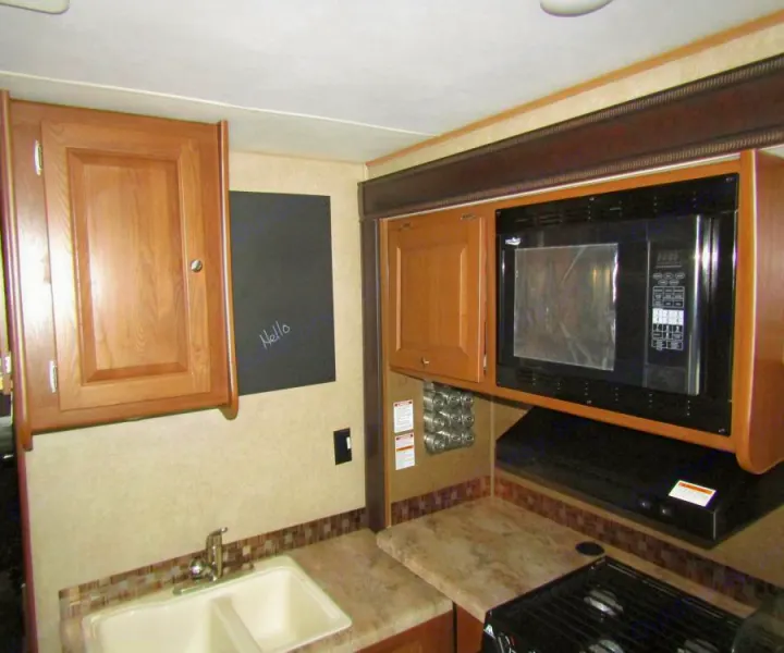 Well-equipped rv rental kitchen featuring a microwave, double sink, and wooden cabinets.. Coachmen Leprechaun 2017