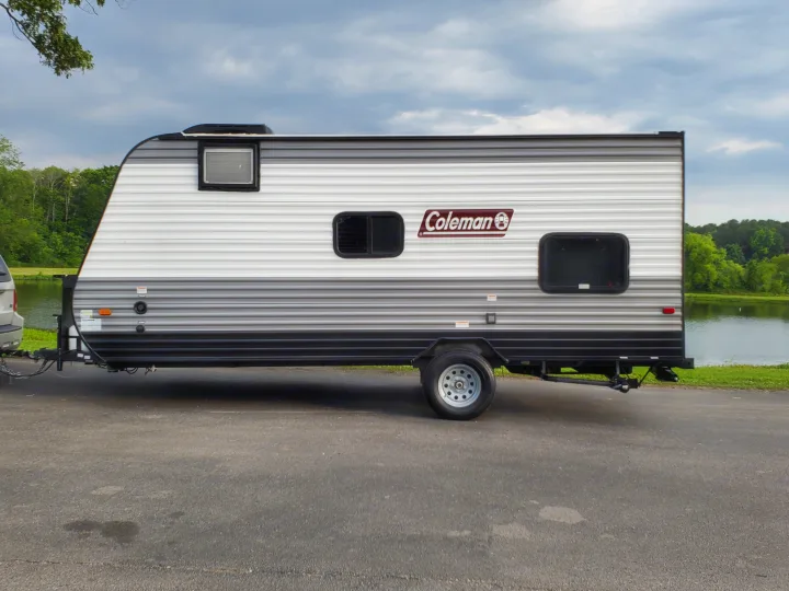 A Coleman travel trailer, ideal for an RV rental, parked by a scenic lake. Perfect for outdoor camping adventures.. Coleman LANTERN LT 17B 2022