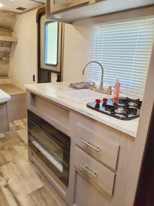 RV rental kitchen area features a sink, gas stovetop, and a cozy electric fireplace. Modern interior.. Coleman LANTERN LT 17B 2022
