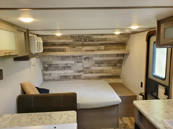 Inside a modern **rv rental**: a cozy bed with wood accent wall, overhead cabinets, AC, and marble countertop. Bright and functional interior.. Coleman LANTERN LT 17B 2022