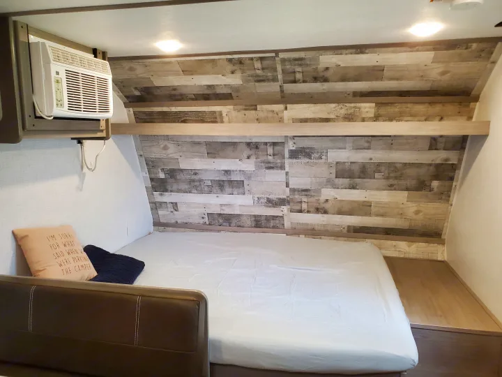 Cozy RV rental bedroom featuring a bed with white sheets, a decorative wood-paneled wall, and an overhead AC unit.. Coleman LANTERN LT 17B 2022