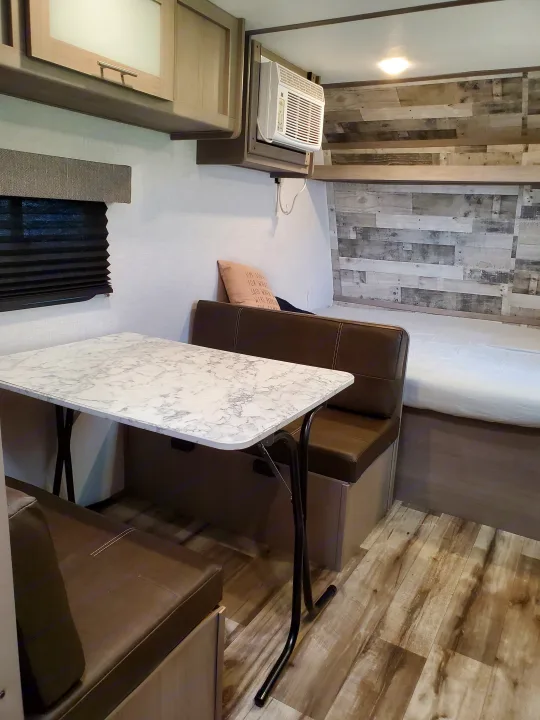 RV rental interior features a cozy dinette with a marble-look table, bed, and wall-mounted AC unit for travel comfort.. Coleman LANTERN LT 17B 2022
