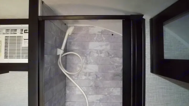 Inside an RV rental: a modern shower with faux grey tiles and an adjacent air conditioner.. Braxton Creek Bushwhacker 2022