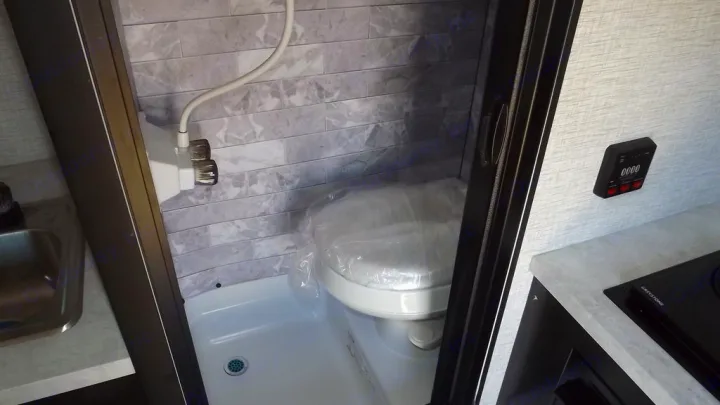 Compact RV rental interior featuring a wet bath with toilet/shower combo, sink, and control panel. Efficient space usage.. Braxton Creek Bushwhacker 2022