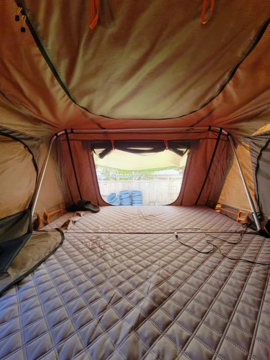 View inside a cozy RV rental rooftop tent: a quilted mattress on the floor and windows showing a backyard fence.. Toyota Tundra 2011
