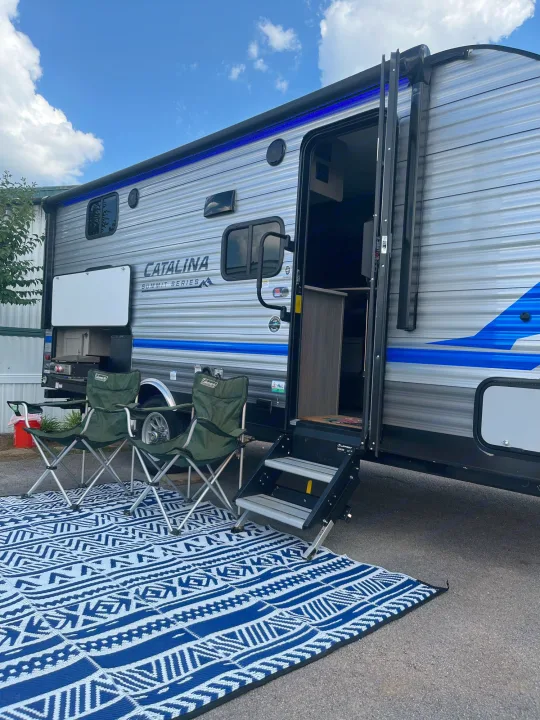 This rv rental offers a comfortable outdoor setup with chairs, a patterned rug, and an outdoor kitchen, ideal for camping trips.. Coachmen Catalina Summit Series 7 2022