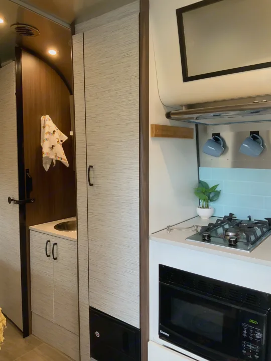 Modern RV rental interior featuring a compact kitchen with stove, microwave, and sink, alongside a bathroom entrance.. Airstream Airstream 2020