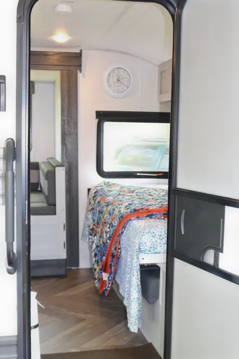 View into an RV rental: features a cozy bedroom area with patterned bedding, kitchenette, and wood-look flooring.. Forest River Wildwood FSX 2021
