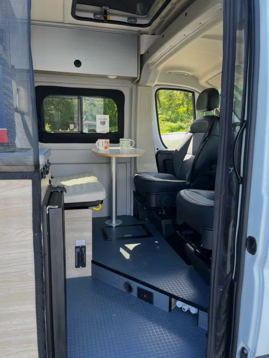 Your next RV rental: a modern camper van interior with a dinette, kitchen, and adaptable seating.. Ram Winnebago Solis 2023